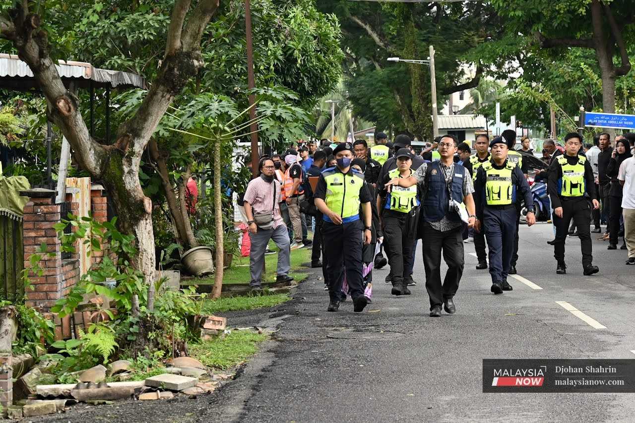 Police officers escort the court bailiff as he goes door to door to serve eviction notices to the residents of Kampung Sungai Baru in Kuala Lumpur.