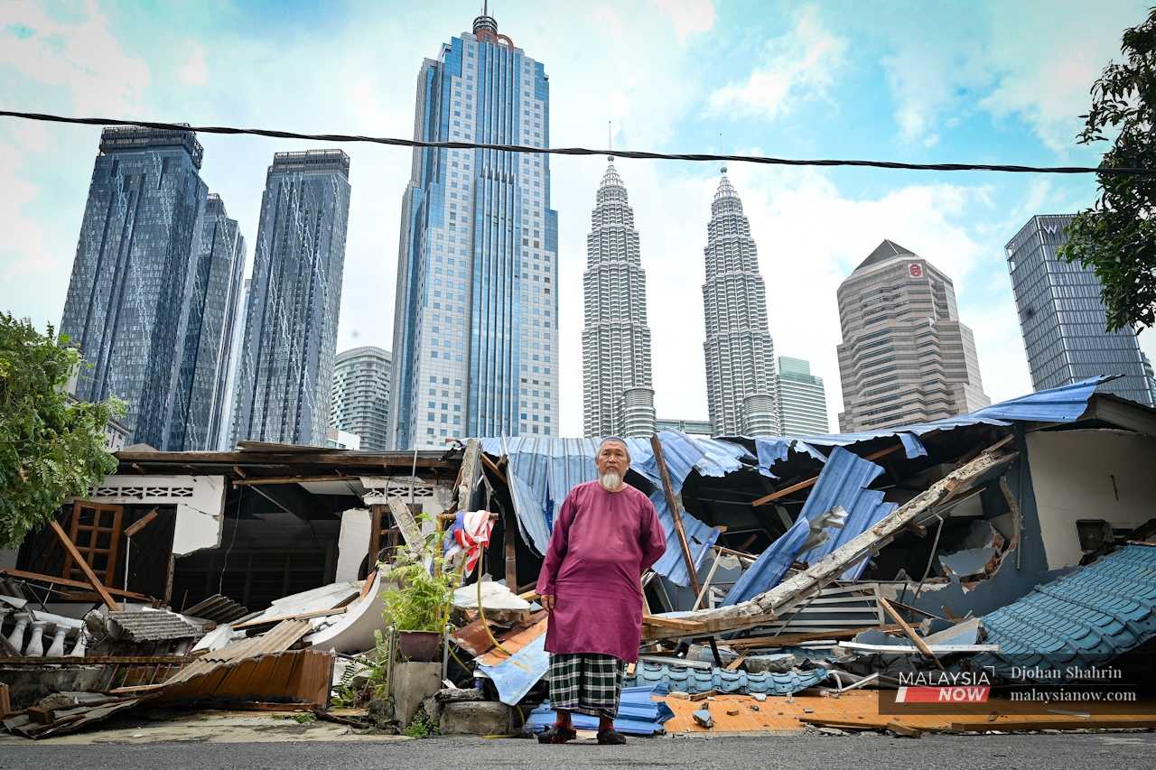 Resident Syukri Kartho stands in front of the rubble and debris that used to be his home, in the once happy village of Kampung Sungai Baru. 